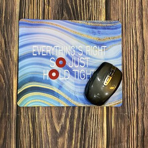 May include: A blue and gold marble mouse pad with the text "Everything's Right So Just Hold Tight". A black wireless mouse is on the mouse pad.