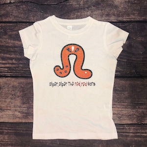 May include: White t-shirt with a red worm graphic and the text "Piper, Piper the red, red worm".