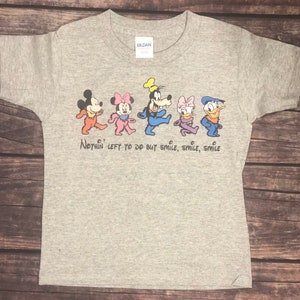 May include: Gray t-shirt with a graphic of Mickey Mouse, Minnie Mouse, Goofy, Daisy Duck, and Donald Duck walking in a line. The text "Nothin' left to do but smile, smile, smile" is printed below the characters.