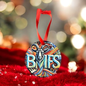 May include: A round, colorful Christmas ornament with a goat head and the letters "BMFS" in a stylized font. The ornament is decorated with musical notes and a rainbow-colored design.