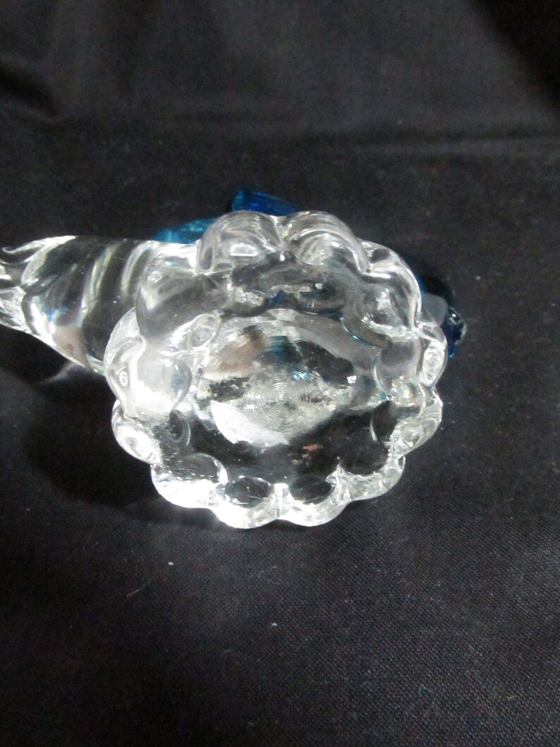 Puede incluir: Un tap&oacute;n de botella de vidrio transparente con una superficie texturizada y con burbujas. El tap&oacute;n tiene un acento de vidrio azul en la parte superior.