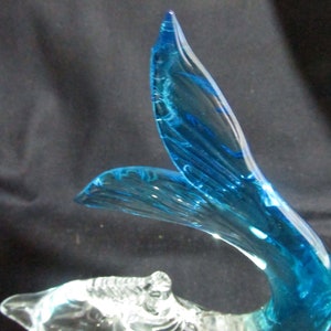 Puede incluir: Una escultura de vidrio de un delf&iacute;n azul con un cuerpo de vidrio transparente. La cola del delf&iacute;n es de un color azul vibrante y tiene un patr&oacute;n de remolino.