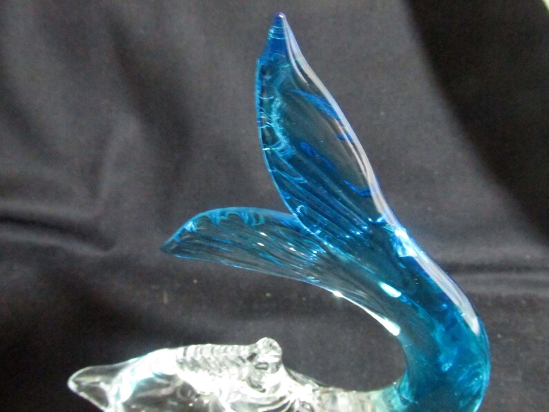 Puede incluir: Una escultura de vidrio de un delf&iacute;n azul con un cuerpo de vidrio transparente. La cola del delf&iacute;n es de un color azul vibrante y tiene un patr&oacute;n de remolino.