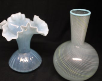 May include: Two glass vases, one with a ruffled, light blue design and the other with a white and light green swirl pattern.