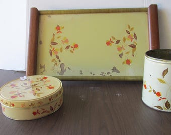 May include: A set of three vintage kitchenware items featuring a floral design. A rectangular tray with a wooden frame, a round canister, and a round cookie tin. All three items have a light green background with a floral pattern in shades of orange, yellow, and brown.
