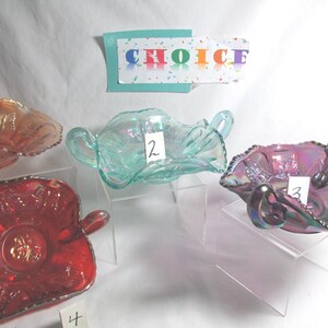 May include: Four iridescent glass serving dishes in shades of orange, teal, and purple. Each dish has a unique shape and design, with handles and decorative edges. A card with the word "CHOICE" is in the background.
