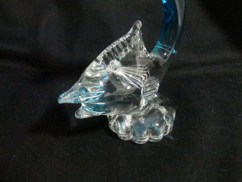 Puede incluir: Una escultura de vidrio de un pez vela azul con una base de vidrio transparente. El pez vela est&aacute; saltando fuera del agua con la cola levantada.