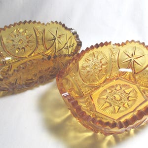 May include: Two amber-colored glass bowls with star and geometric patterns. The bowls have a scalloped edge and are likely vintage or antique decorative pieces. The glass has a textured, cut-glass appearance.