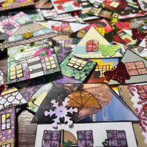 May include: A collection of colorful, handmade paper houses with various patterns and textures. Some houses feature butterfly and snowflake embellishments. The houses have different roof shapes and window designs, creating a whimsical and artistic display.