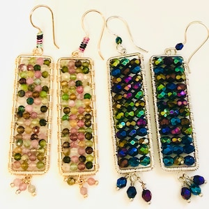 Puede incluir: Cuatro pares de pendientes colgantes rectangulares. Dos pares presentan una mezcla de cuentas rosas, verdes y marrones, mientras que los otros dos muestran cuentas iridiscentes azules y verdes. Todos los pendientes tienen marcos de alambre dorados y ganchos plateados.