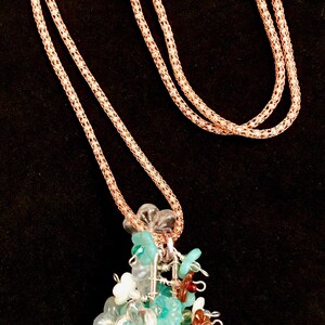 May include: A rose gold necklace with a delicate chain and a floral pendant. The pendant features clear, turquoise, and brown flower-shaped beads, along with green and clear beads. The necklace has a toggle clasp.