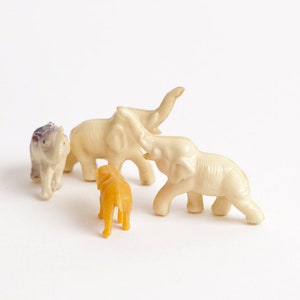 May include: A set of four toy elephants, three are white and one is purple. The elephants are standing on a white surface. There is also a small orange toy elephant in the center of the image.