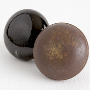 May include: Two round knobs, one black and one brown. The black knob is smooth and shiny, while the brown knob is textured and dull.