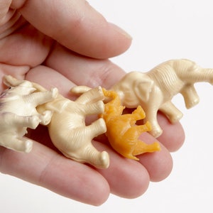 May include: A collection of four small plastic toy elephants. Three of the elephants are white and one is orange.
