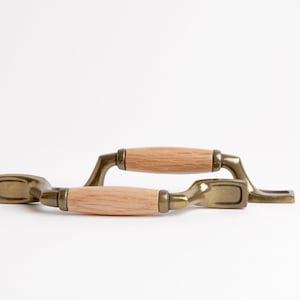 Könnte beinhalten: Zwei antike Messing-Schrankgriffe mit Holzgriffen. Die Griffe haben eine rechteckige Form mit einem gebogenen Holzgriff.