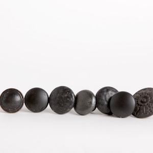 May include: A row of seven black cabinet knobs with a variety of designs, including round, square, and ornate.