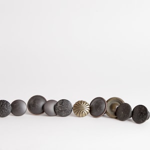 May include: A row of eight round black and brass cabinet knobs. The knobs are arranged in a line, with the black knobs on the left and the brass knobs on the right.
