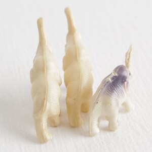 May include: Three small plastic toy elephants, two are white and one is white with purple accents.