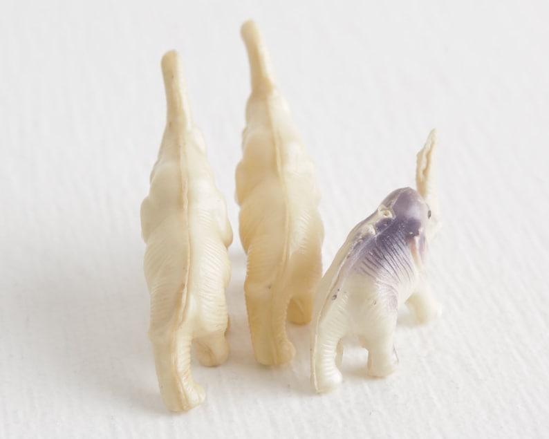 May include: Three small plastic toy elephants, two are white and one is white with purple accents.