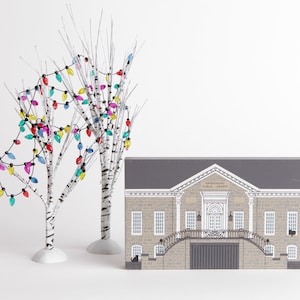 May include: Two white birch trees with colorful string lights wrapped around the branches. A gray wooden sign with the text "Hanover Public Library" is in the foreground.