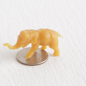 May include: A small, yellow plastic toy elephant figurine. The elephant is standing on a US quarter.