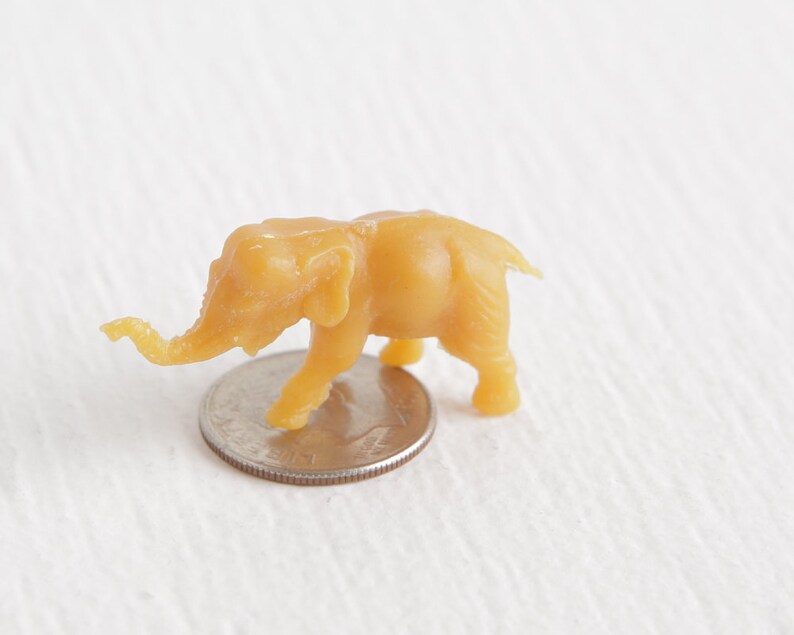 May include: A small, yellow plastic toy elephant figurine. The elephant is standing on a US quarter.