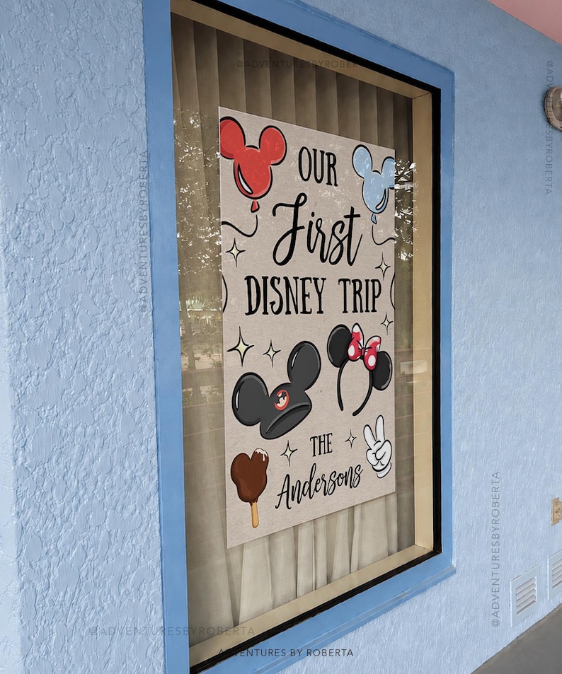 May include: A framed sign with the text "OUR First DISNEY TRIP" and "THE Andersons". The sign features Mickey Mouse and Minnie Mouse ears, a Mickey ice cream bar, and a peace sign. The sign is displayed in a window with a blue frame.