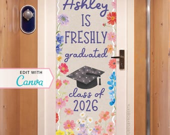 May include: A graduation door sign with the text "Ashley IS FRESHLY graduated class of 2026" surrounded by colorful flowers. The sign is on a door with a decorative handle and a small nautical-themed wall decoration.