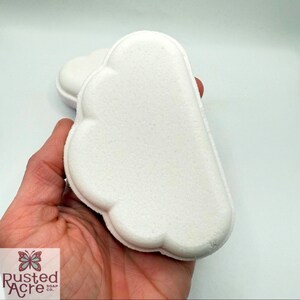 A handmade rainbow cloud bath bomb by Rusted Acre Soap Co. in a hand.