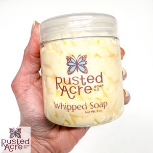 A jar of yellow whipped soap handmade by Rusted Acre Soap Co in a hand.