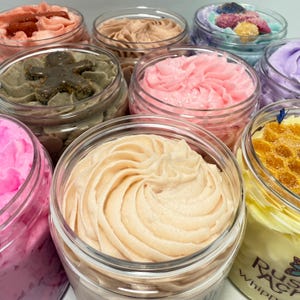 Top of various jars of fluffy handmade whipped soap from Rusted Acre Soap Co. Yellow, peach, pink, purple, teal, red.