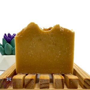 May include: A bar of handmade soap with a light brown color and a rough texture. The soap is sitting on a wooden soap dish.