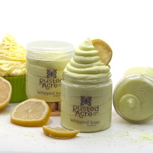 May include: Two clear plastic jars of pale yellow whipped soap with a butterfly logo and the text Rusted Acre Soap Co. Whipped Soap Net Wt. 8 oz. One jar is topped with a swirl of soap and a lemon slice. Nearby are lemon slices and a cupcake.