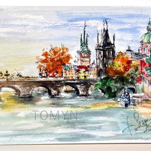 May include: Watercolor painting of a bridge over a river with buildings and trees in the background. The buildings have red, green, and brown roofs. The trees are a mix of green and orange. The bridge is made of stone and has arches. The river is blue and the sky is light blue. The painting is signed "Tomyn" in the bottom left corner and "Prague" in the bottom right corner.