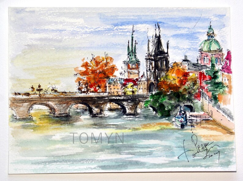 May include: Watercolor painting of a bridge over a river with buildings and trees in the background. The buildings have red, green, and brown roofs. The trees are a mix of green and orange. The bridge is made of stone and has arches. The river is blue and the sky is light blue. The painting is signed "Tomyn" in the bottom left corner and "Prague" in the bottom right corner.