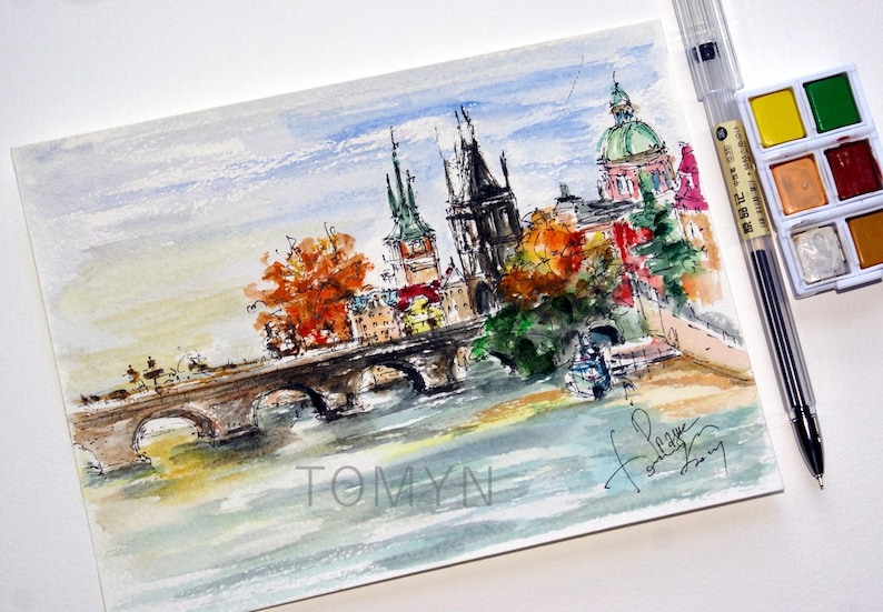 May include: Watercolor painting of a cityscape with a bridge, river, and buildings. The buildings have colorful roofs and there are trees in the foreground. The painting is signed "Tomyn" in the bottom left corner and "for love" in the bottom right corner.