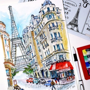 May include: Watercolor painting of a Parisian street scene with the Eiffel Tower in the background. The painting features a cafe with a red awning and a building with a yellow facade. The painting is signed "TOMYN" and dated "2018".