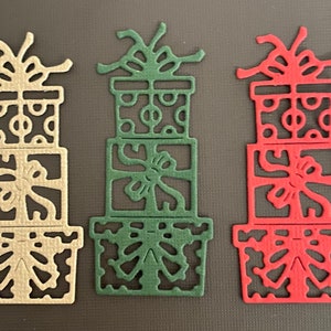 May include: Three stacked gift boxes with bows, one in beige, one in green, and one in red. The boxes are intricately cut out with a decorative design.
