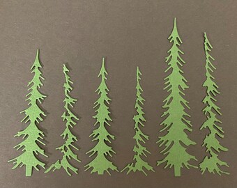 May include: Seven green paper cutouts of pine trees in various sizes, arranged in a row on a brown background.