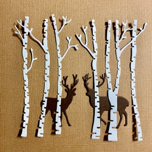May include: White paper cutouts of birch trees with two brown paper cutouts of deer standing behind the trees.