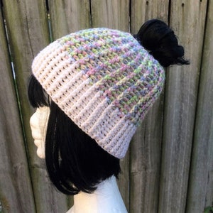 May include: A white and pastel-coloured crochet beanie with a messy bun space at the back.