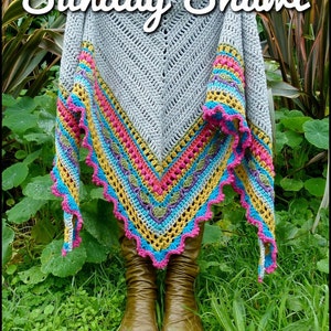 Pode incluir: Um xale de croch&ecirc; cinza com uma borda colorida em tons de rosa, amarelo, azul e verde. O xale est&aacute; drapeado sobre os ombros de uma pessoa e as pontas est&atilde;o penduradas. O xale tem uma borda festonada.