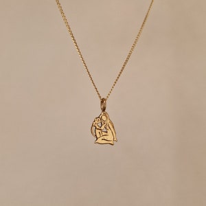 Puede incluir: Un collar de cadena de oro con un colgante que presenta un diseño recortado de dos figuras abrazándose. El colgante es un diseño simple y elegante.