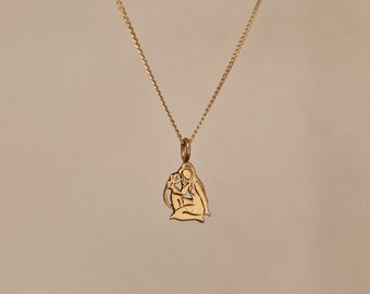 May include: A gold chain necklace with a pendant featuring a cutout design of two figures embracing. The pendant is a simple, elegant design.