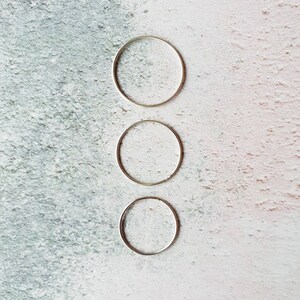 May include: Three silver rings of different sizes stacked on top of each other against a white and grey textured background.