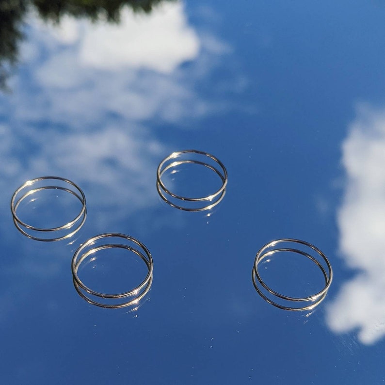 Puede incluir: Cuatro anillos plateados sobre un fondo azul. Los anillos son simples y delicados, con un acabado liso.