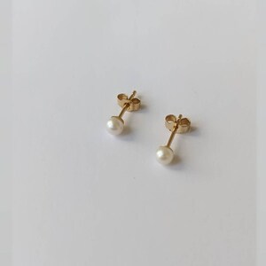 May include: A pair of gold stud earrings with small white pearl accents.