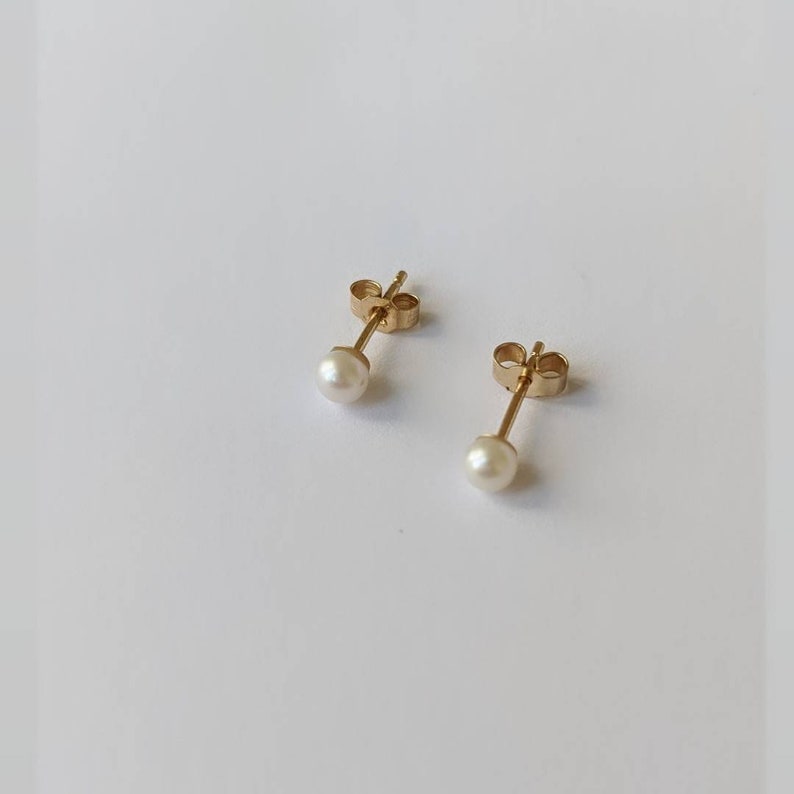 May include: A pair of gold stud earrings with small white pearl accents.