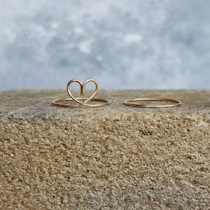 Puede incluir: Dos anillos de oro sobre una superficie rugosa y marr&oacute;n. Un anillo es una banda simple, el otro tiene forma de coraz&oacute;n.