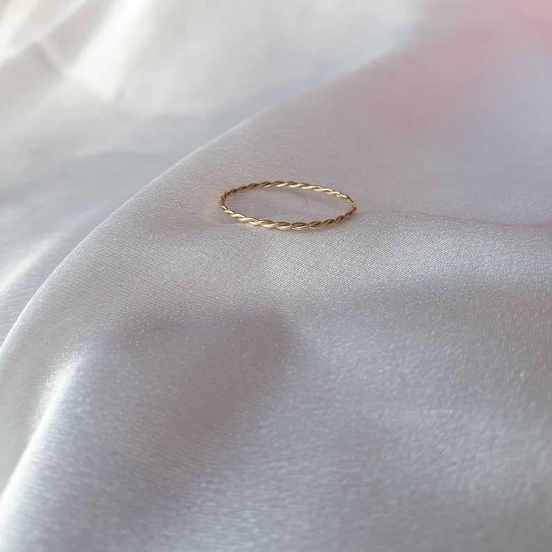 Op de afbeelding: Een eenvoudige gouden ring met een gedraaid ontwerp. De ring ligt op een witte stoffen achtergrond.